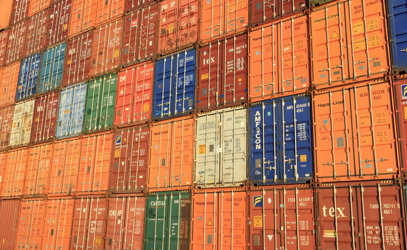 Stacked shipping containers at a global port illustrating education publishing tariffs, tariffs news, and tariff price increases impacting educational supply chains