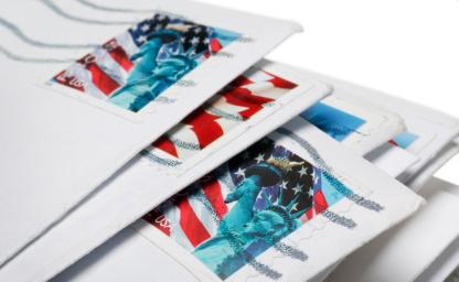 Stack of mailed envelopes with USPS Forever stamps featuring the Statue of Liberty and the American flag, symbolizing rising postage rates and cost-saving opportunities through USPS incentives.